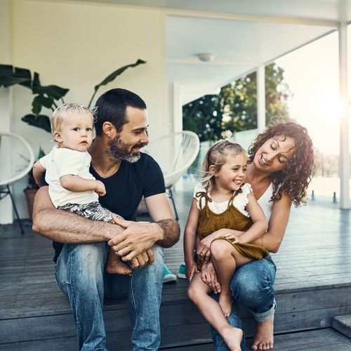 Man and woman both holding a child sitting outdoor porch on dark gray wooden floor with beige walls